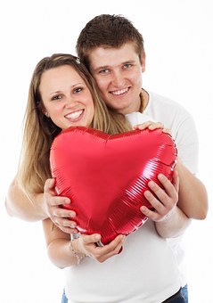 A happy and smiling couple holding a red, heart shaped balloon. 